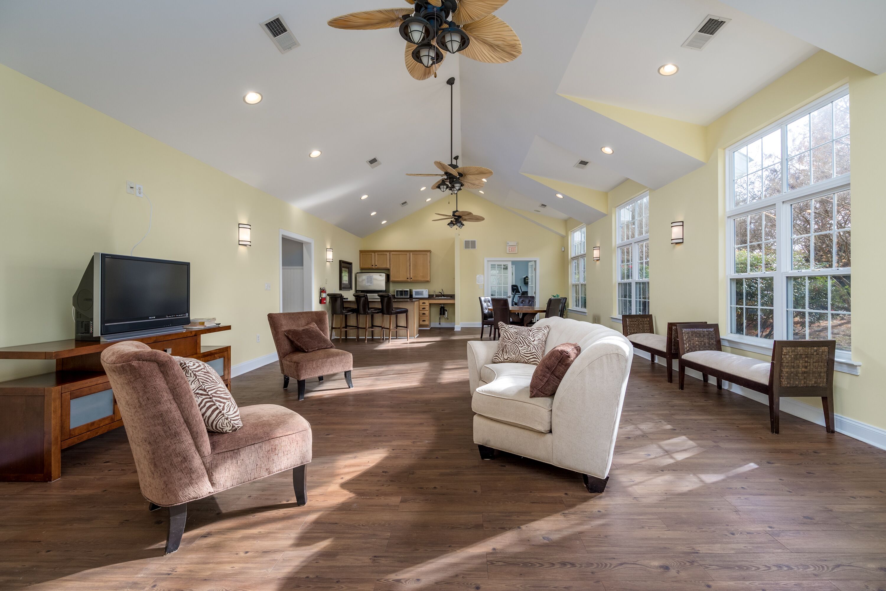 A spacious living room with a large TV, comfortable seating, and a kitchen in the background.