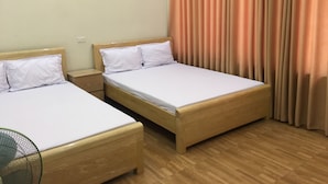 Two single beds with wooden frames and white bedding, a nightstand, and a standing fan.