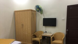 A room with two beds, a wardrobe, a TV, a fan, and two wicker chairs.