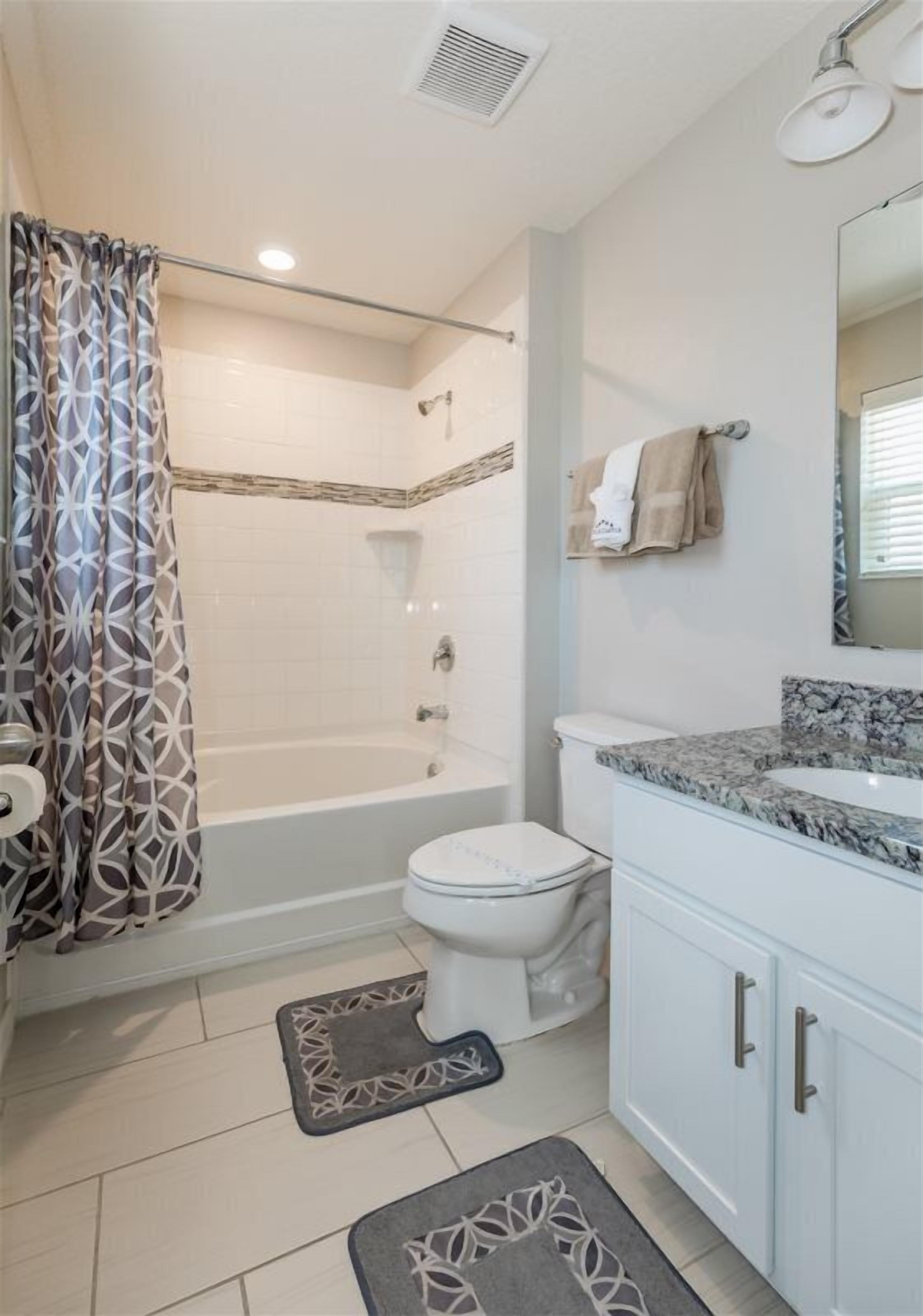 Un baño con ducha, inodoro y lavamanos, que presenta una cortina de baño estampada y un perchero.