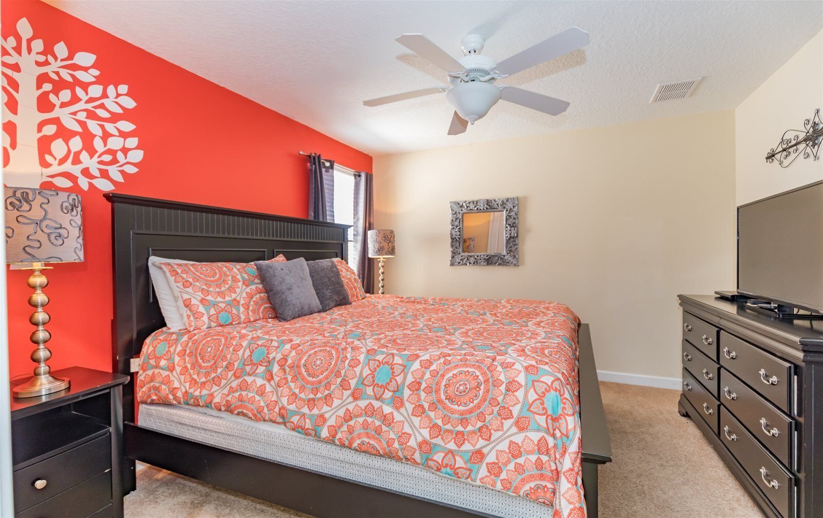 A bedroom with a bed, nightstands, a dresser, a ceiling fan, and a wall with a decorative piece.