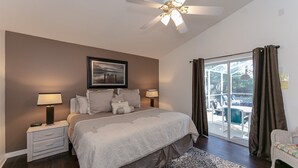 Ein Schlafzimmer mit einem großen Bett, zwei Nachttischlampen, einem Deckenventilator, einem gerahmten Bild und Blick ins Freie durch eine Schiebetür.