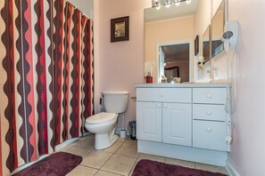 A bathroom with a white toilet, a white vanity with drawers, a mirror, and a shower curtain with a wavy pattern. - Windsor_palms_102 (Kissimmee)
