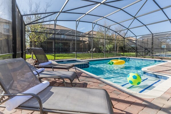 An outdoor swimming pool with a covered area, lounge chairs, and a hot tub.