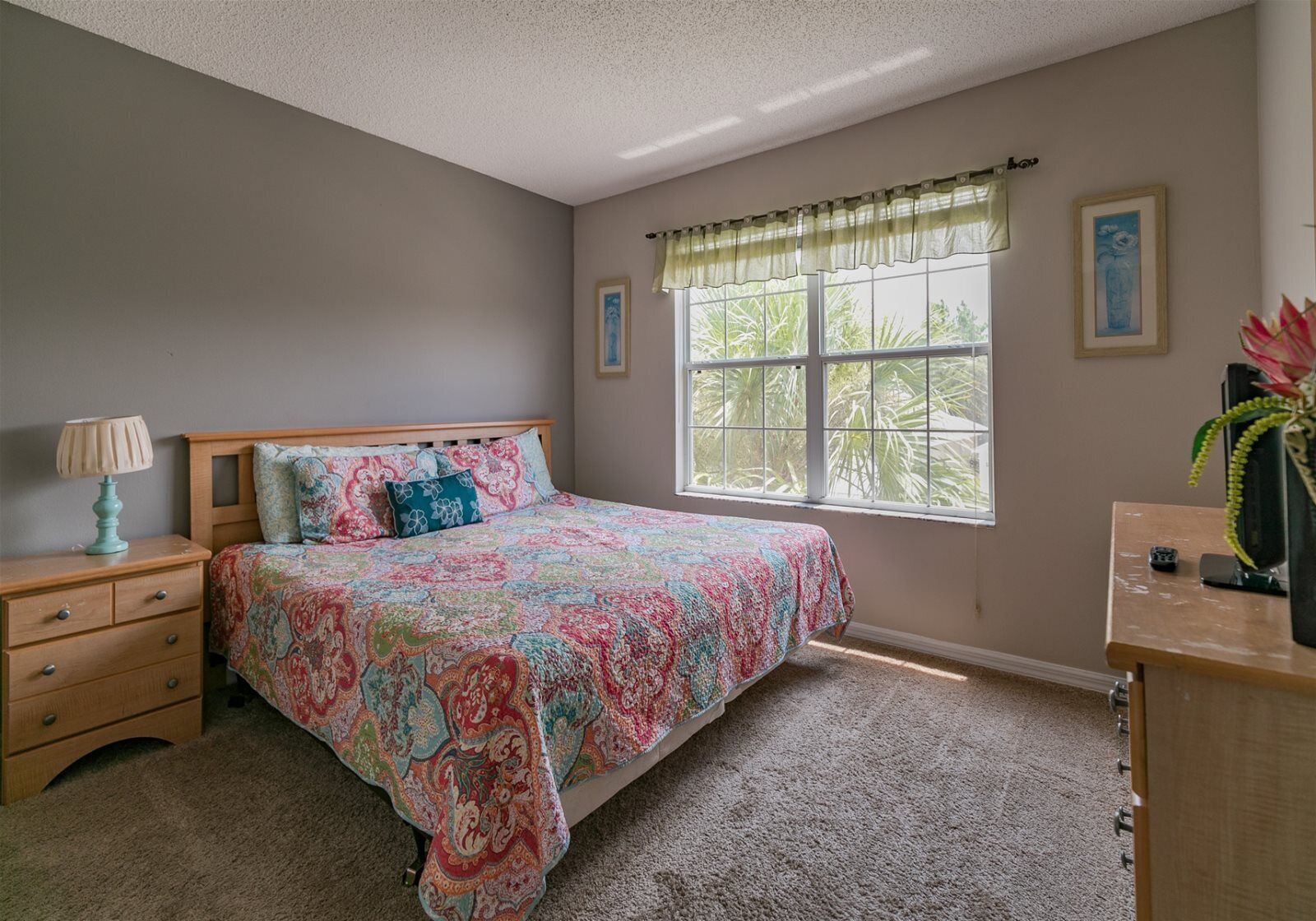 A bedroom with a bed, a nightstand, a dresser, a window with curtains, and a framed picture on the wall.