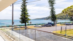 A balcony with a view of a coastal road, parked cars, and a clear sky. - Shoal Towers, Unit 2 11 Shoal Bay Rd Air Conditioning Wifi free Netflix water views (Shoal Bay)