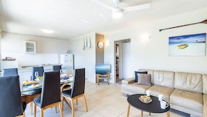 A modern living room with a beige sofa, a dining area with a glass table, and a kitchen in the background. - Shoal Towers, Unit 2 11 Shoal Bay Rd Air Conditioning Wifi free Netflix water views (Shoal Bay)
