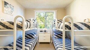 A dormitory room with bunk beds, a bedside table with a lamp, and a window with a view of trees. - Shoal Towers, Unit 2 11 Shoal Bay Rd Air Conditioning Wifi free Netflix water views (Shoal Bay)