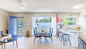 A modern kitchen with a dining area, a blue door, and a view of a building through the window. - Shoal Towers, Unit 2 11 Shoal Bay Rd Air Conditioning Wifi free Netflix water views (Shoal Bay)