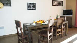 Uma área de refeições com uma mesa de madeira, quatro cadeiras e itens de café da manhã. Há duas molduras na parede.