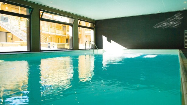 Piscina interior com água cristalina, janelas amplas e uma escada.