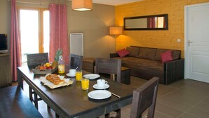 Un área de comedor con una mesa de madera dispuesta para el desayuno, un sofá y un televisor en una esquina.