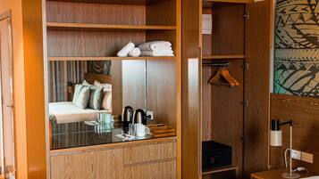 A hotel room with a bed, a wardrobe, a mirror, a desk with a lamp, and a hanging coat rack.