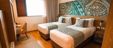 A hotel room with two beds, a desk, and a large abstract wall art piece.