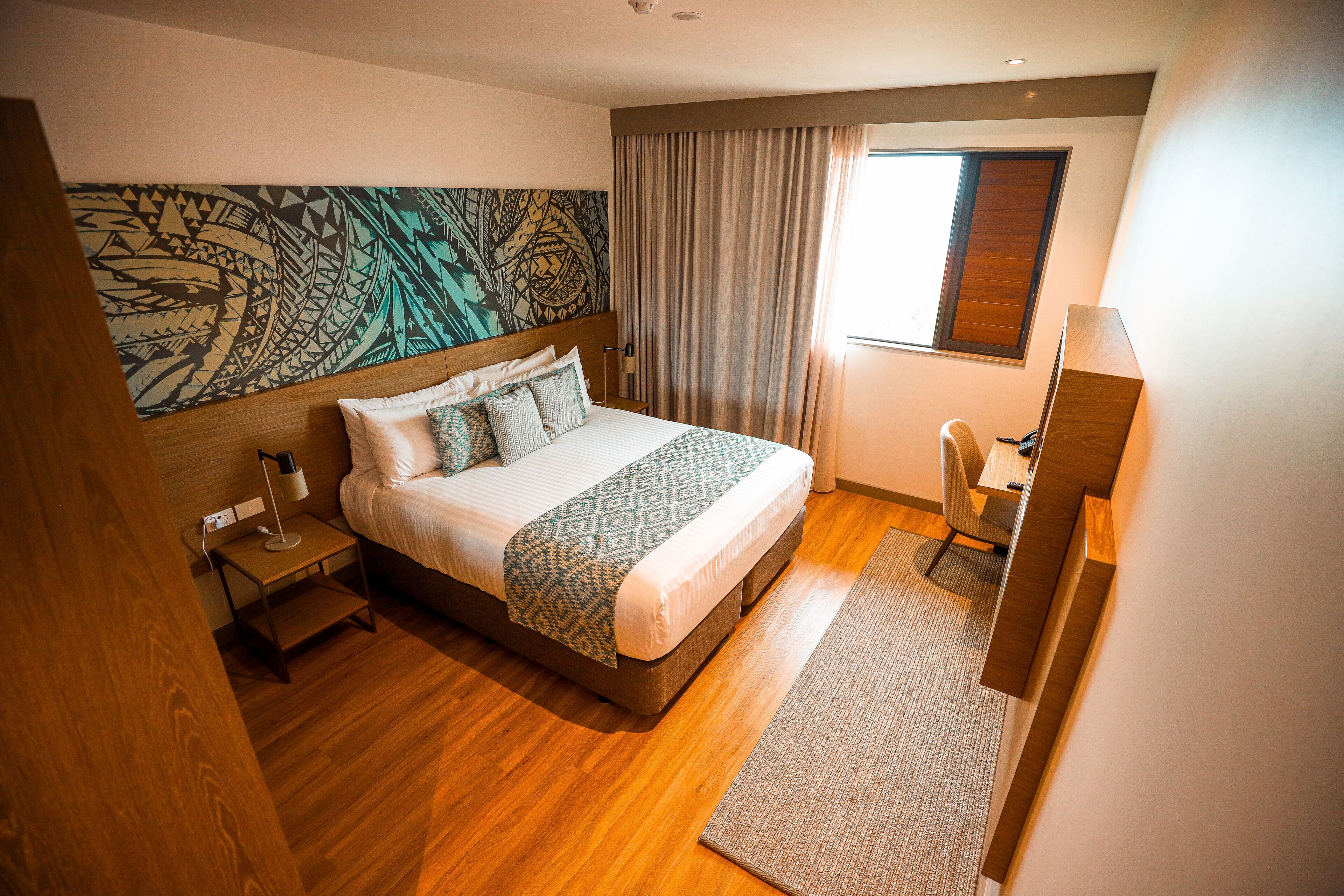 A modern hotel room with a large bed, a desk, and a window with curtains.