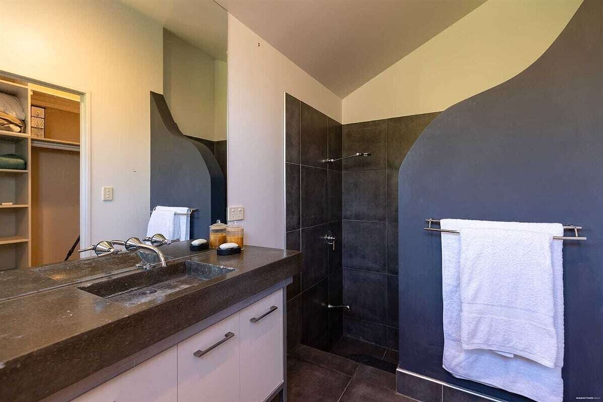 Une salle de bain moderne avec une douche aux carreaux foncés, un lavabo en granit et une serviette blanche suspendue à un porte-serviettes.