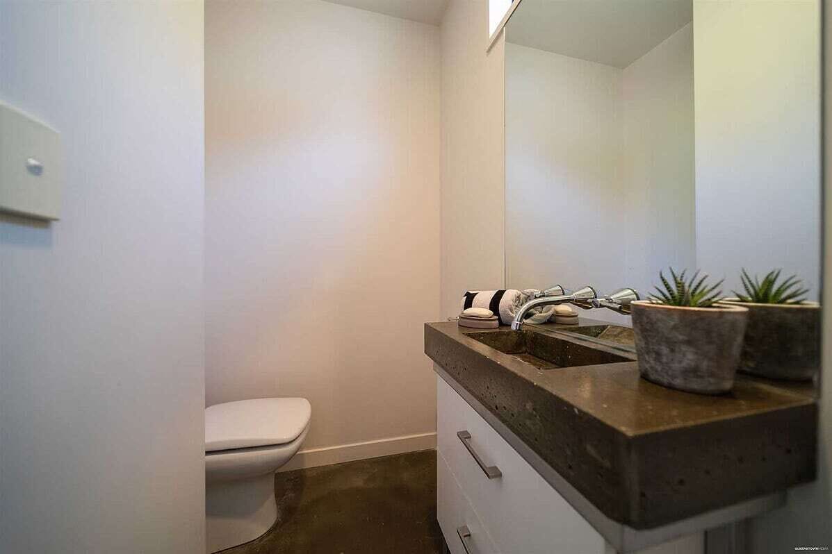 A bathroom with a white toilet, a sink with a dark countertop, and two potted plants on the sink.