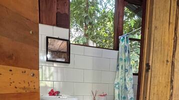 A small bathroom with a wooden floor, white tiles, a sink, a toilet, and a shower curtain.
