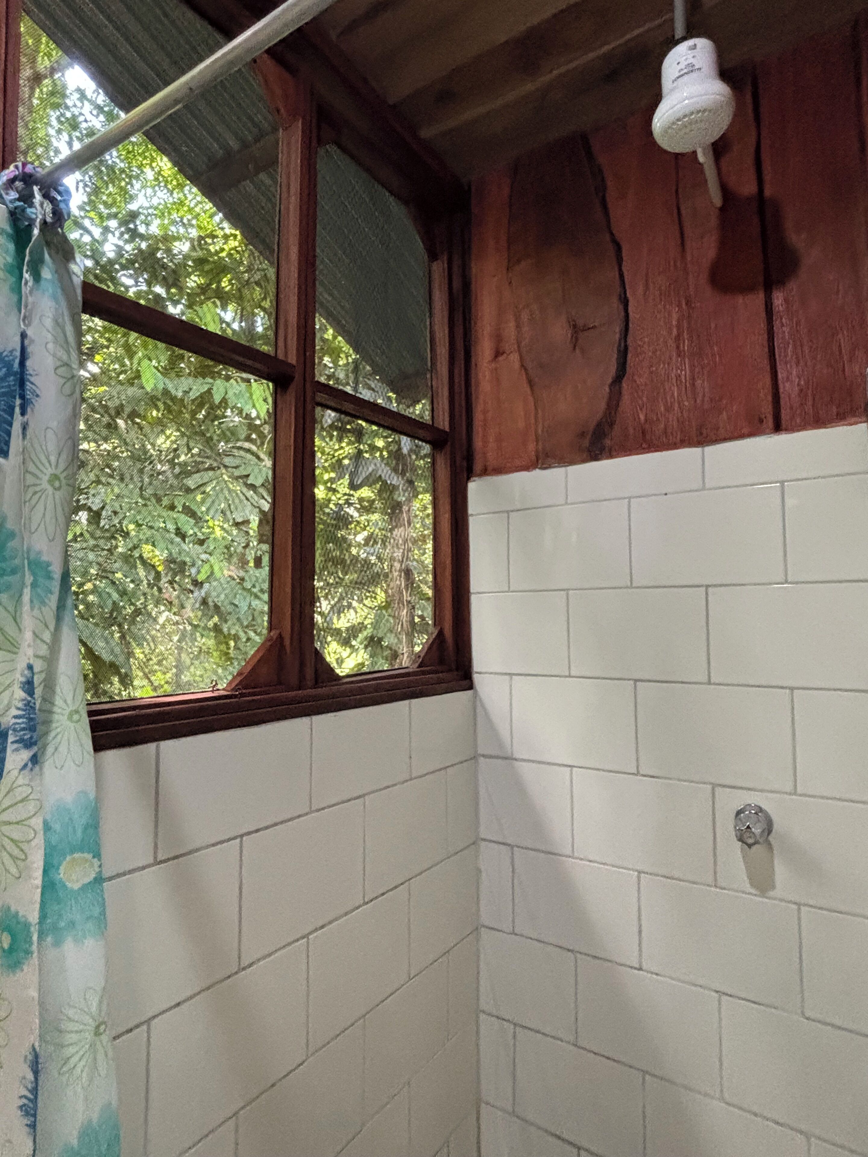 A bathroom with white tiled walls, a wooden window frame, and a shower curtain.
