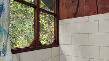 A bathroom with white tiled walls, a wooden window frame, and a shower curtain.