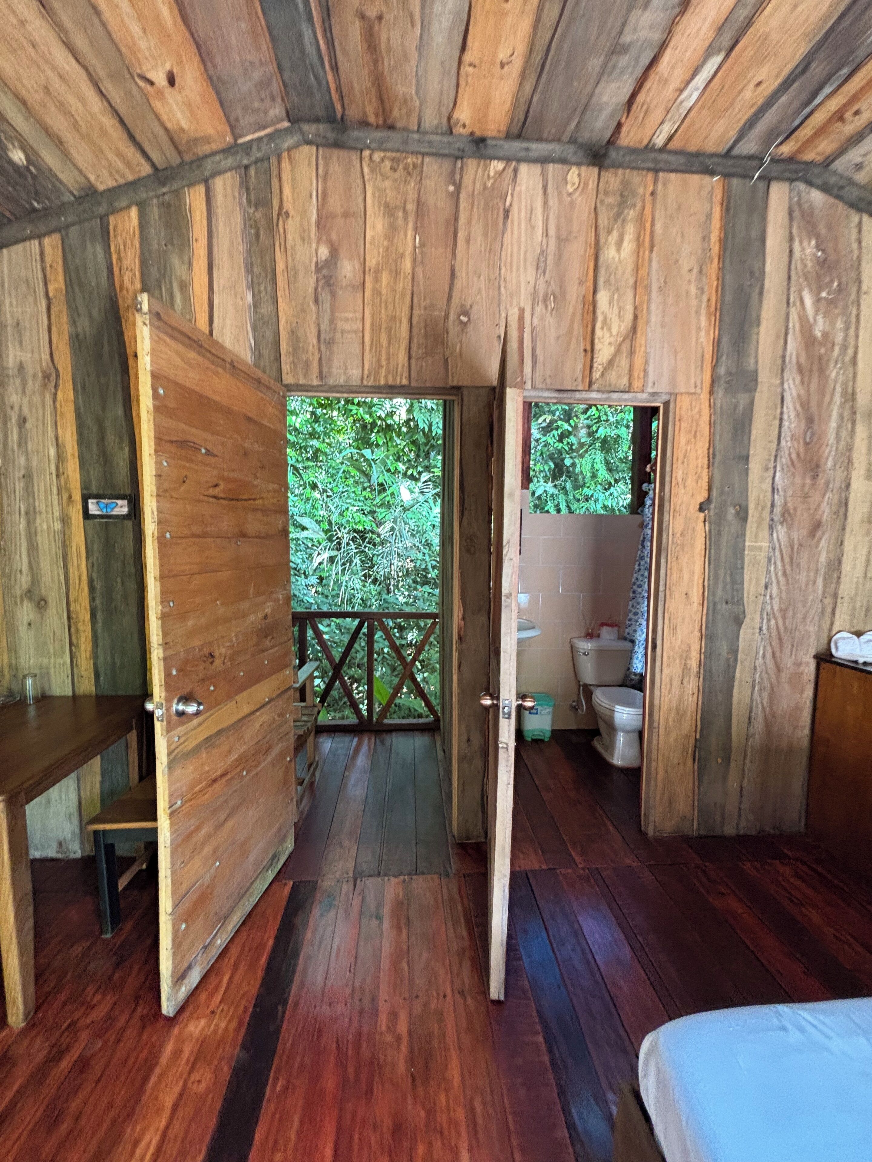 Une cabane en bois avec un plancher en bois, un lit, une table et des toilettes.
