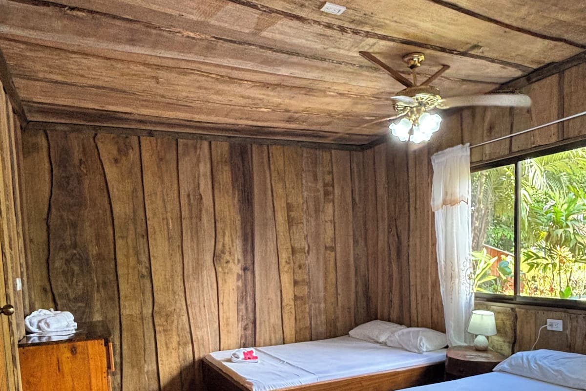 Habitación de madera con dos camas, un armario de madera y una ventana que da a zonas verdes.