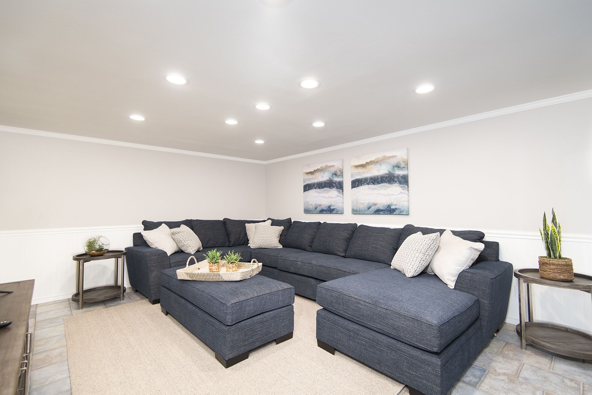 A modern living room with a dark grey sectional sofa, a small coffee table, and two side tables with decorative items.
