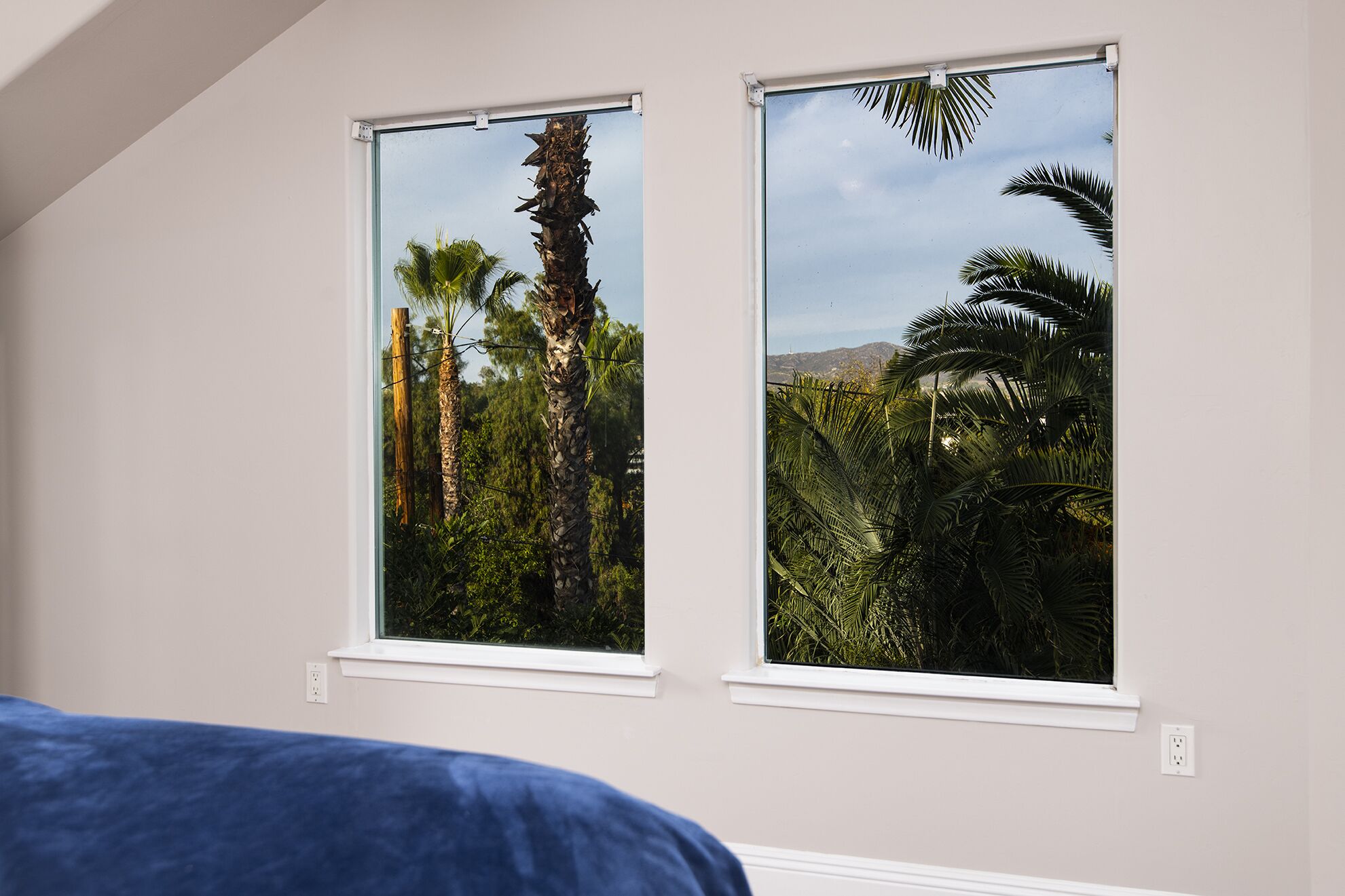 Une chambre à coucher avec deux fenêtres donnant sur un paysage tropical.