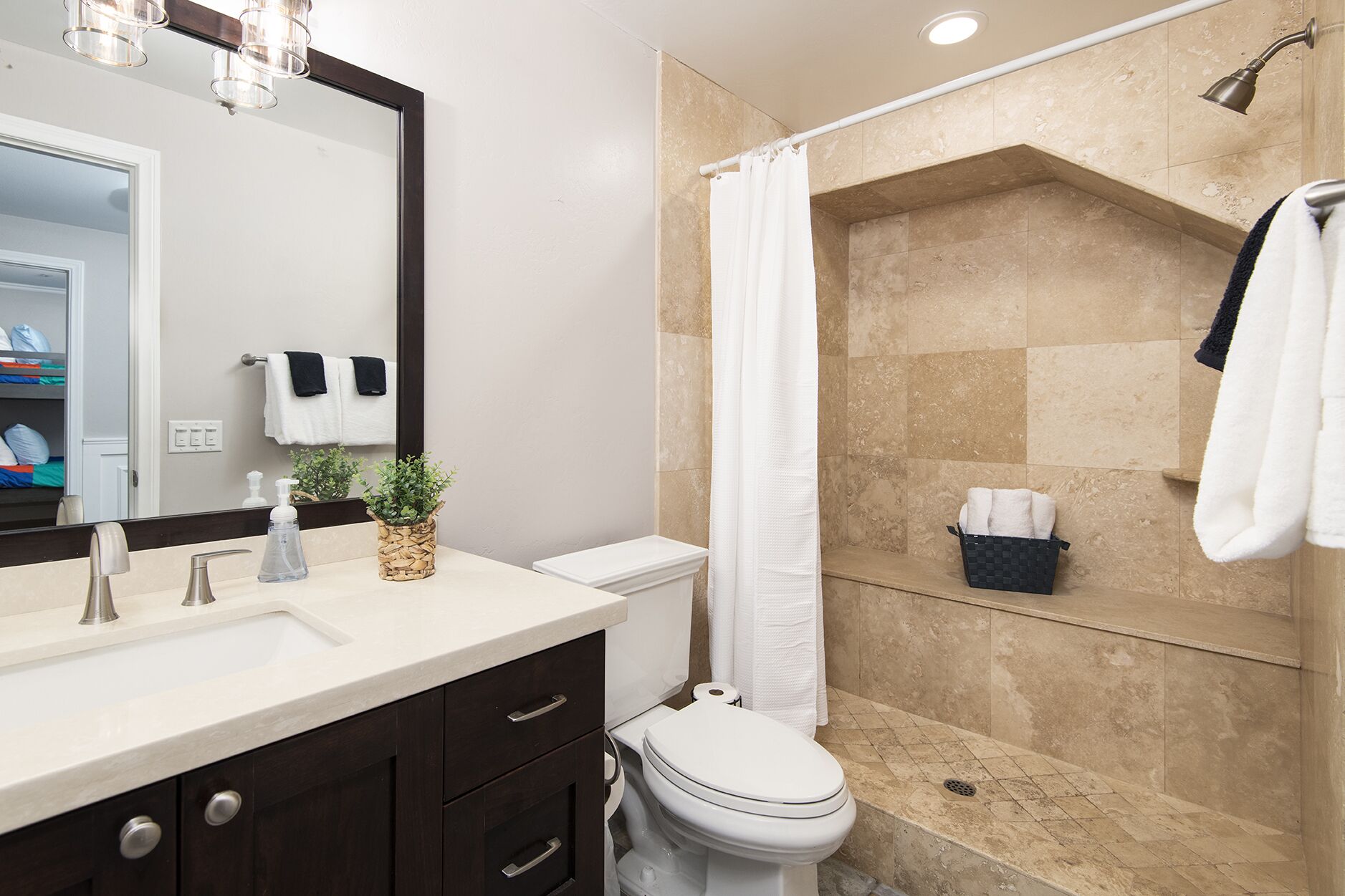 Un bagno moderno con lavandino, specchio e water. Presenta una doccia con pareti piastrellate color beige e tenda da doccia bianca.