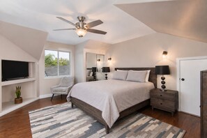 Une chambre avec un lit, une chaise, un téléviseur, un ventilateur de plafond et une fenêtre.