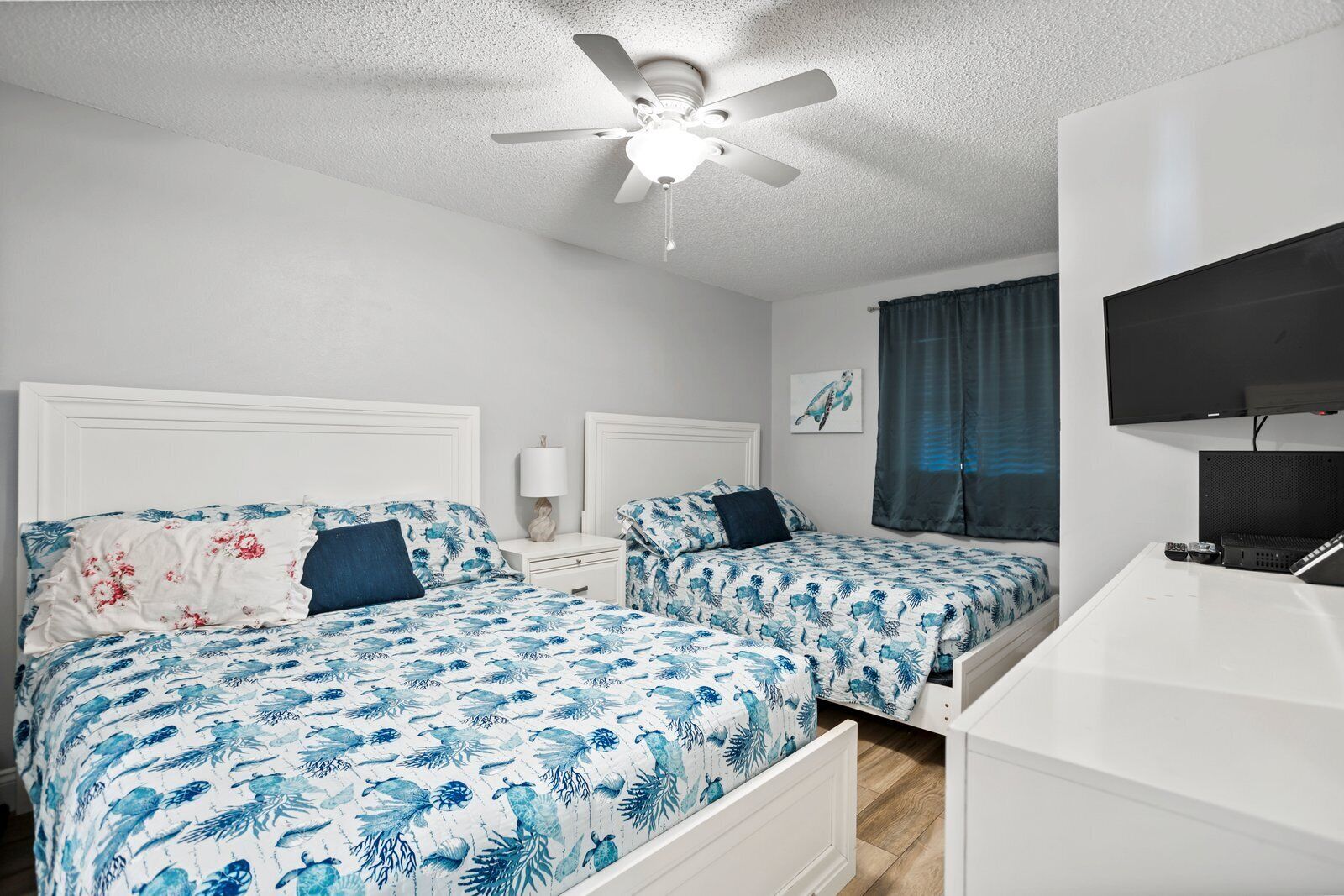 A bedroom with two beds, a ceiling fan, a TV, and a desk.