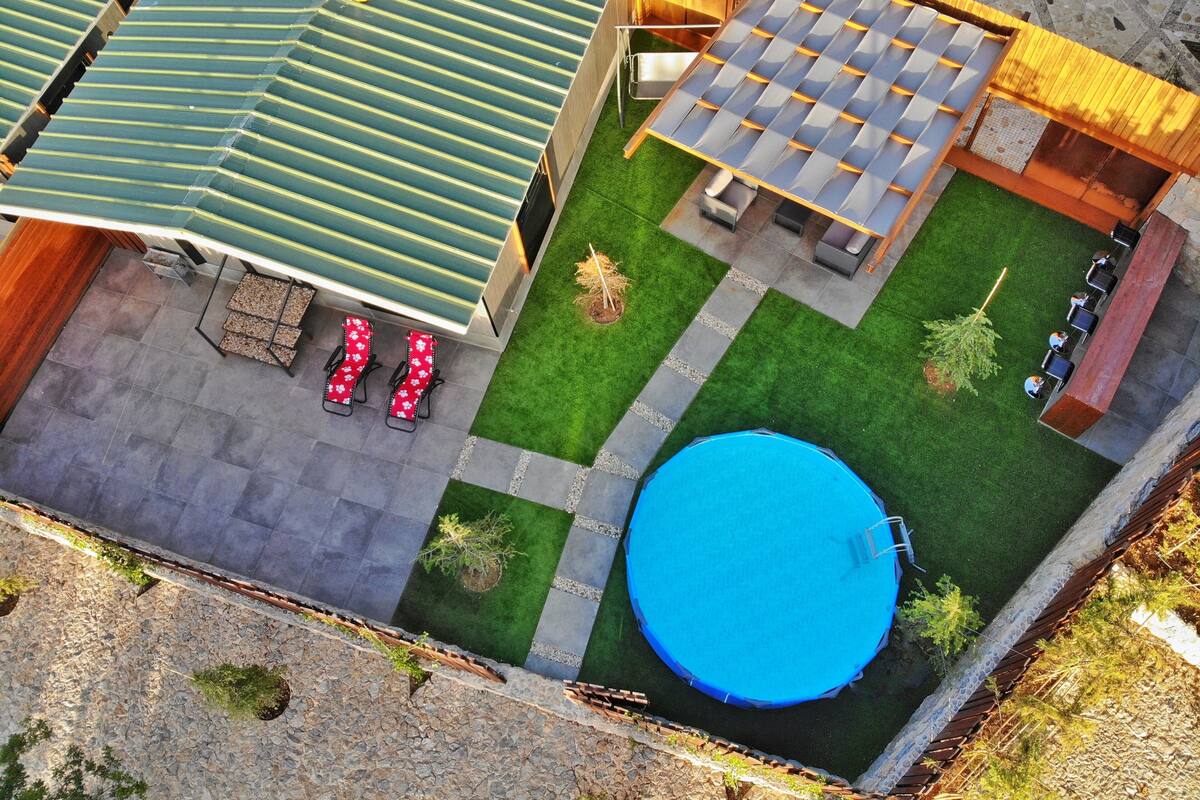 Una piscina en la azotea con cubierta azul, césped verde y terraza de madera con mobiliario exterior.