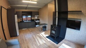 A compact living space with a kitchenette, a sofa, a TV mounted on the wall, and a fireplace. - The Getaway (Hrajel)
