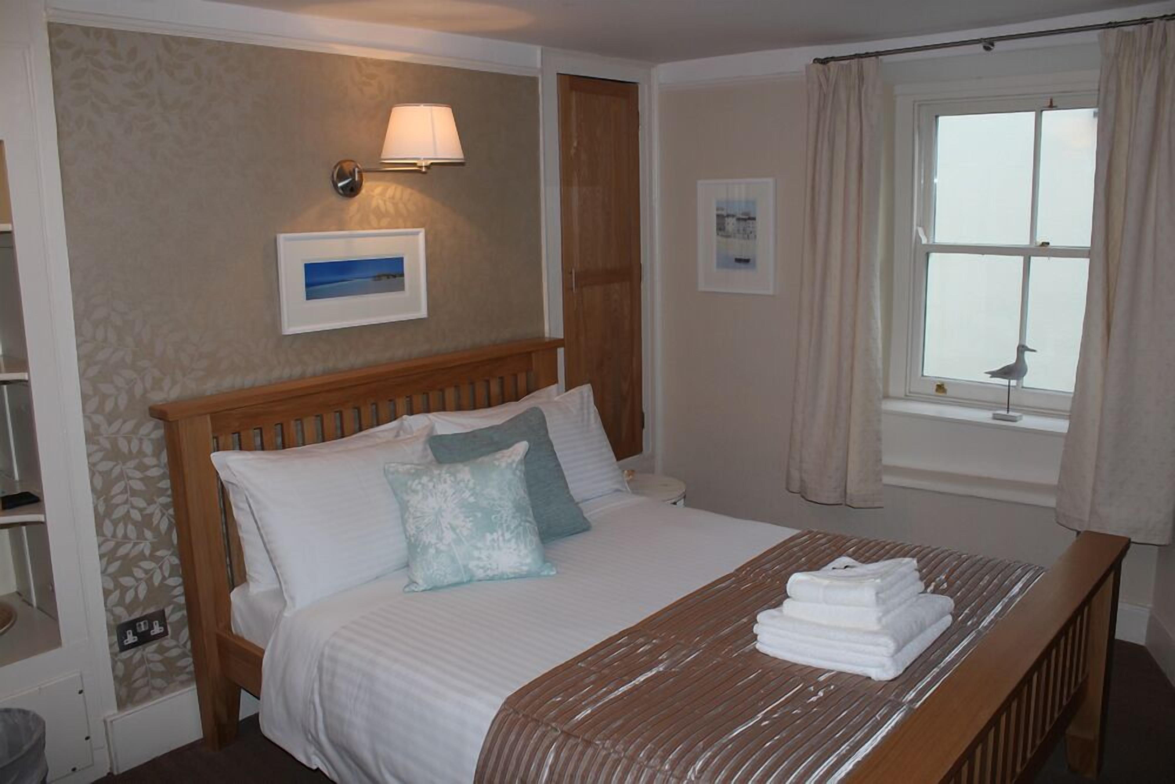 A neatly made bed with pillows, a bedside lamp, and a window with curtains.