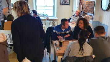 A cozy dining area with patrons seated at tables, a stone wall, and a ceiling-mounted smoke detector.