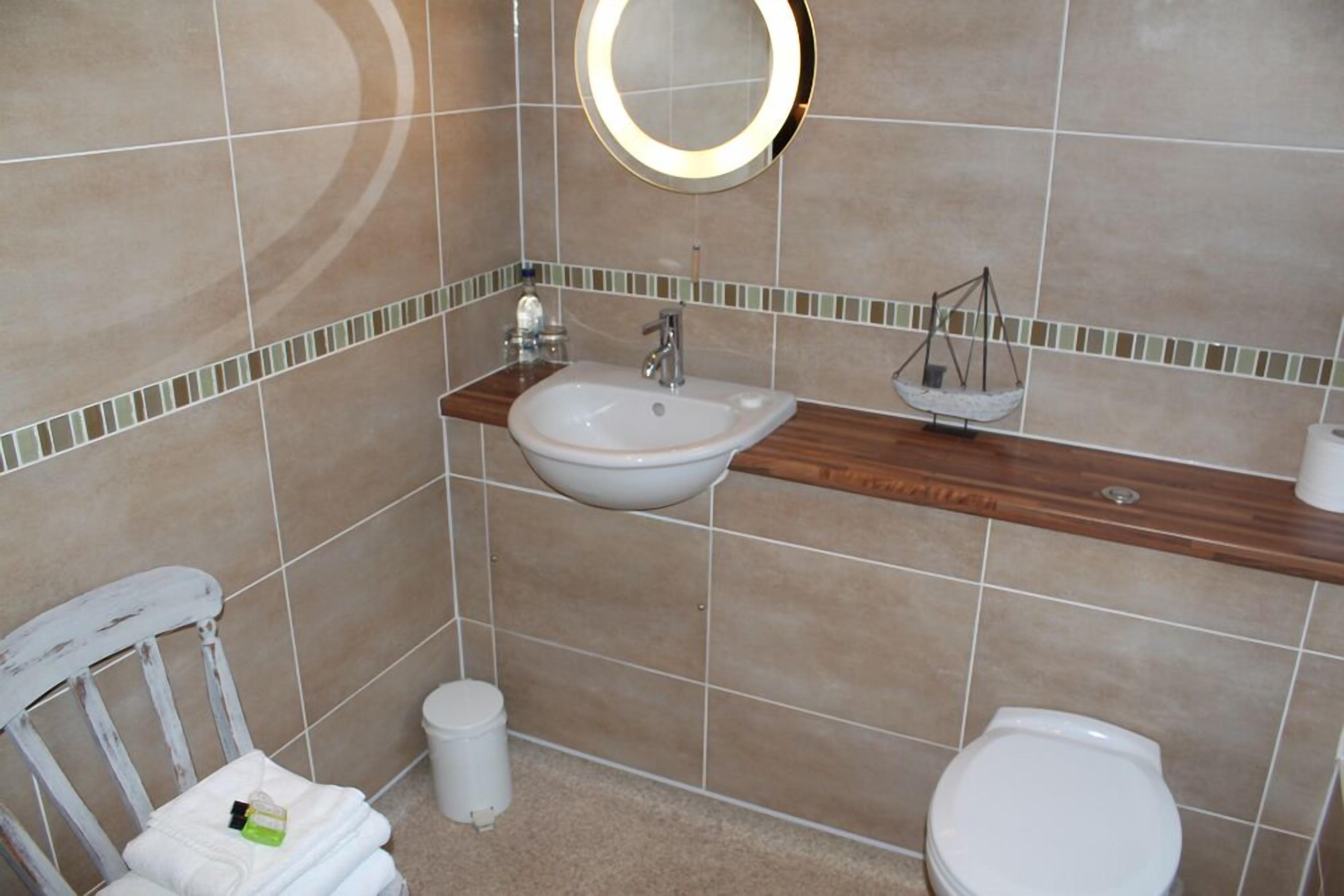 A bathroom with a white sink, wooden vanity, a round mirror, a white toilet, and a small trash bin.