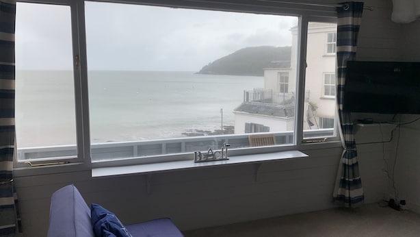 A room with a large window overlooking a coastal view, a bed, and a television mounted on the wall. - Halfway House Inn (Torpoint)