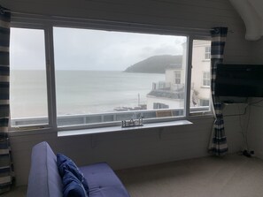 A room with a large window overlooking a coastal view, a bed, and a television mounted on the wall.