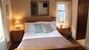 A neatly made bed with a wooden headboard, two bedside tables with lamps, a mirror above the bed, and a window with curtains.