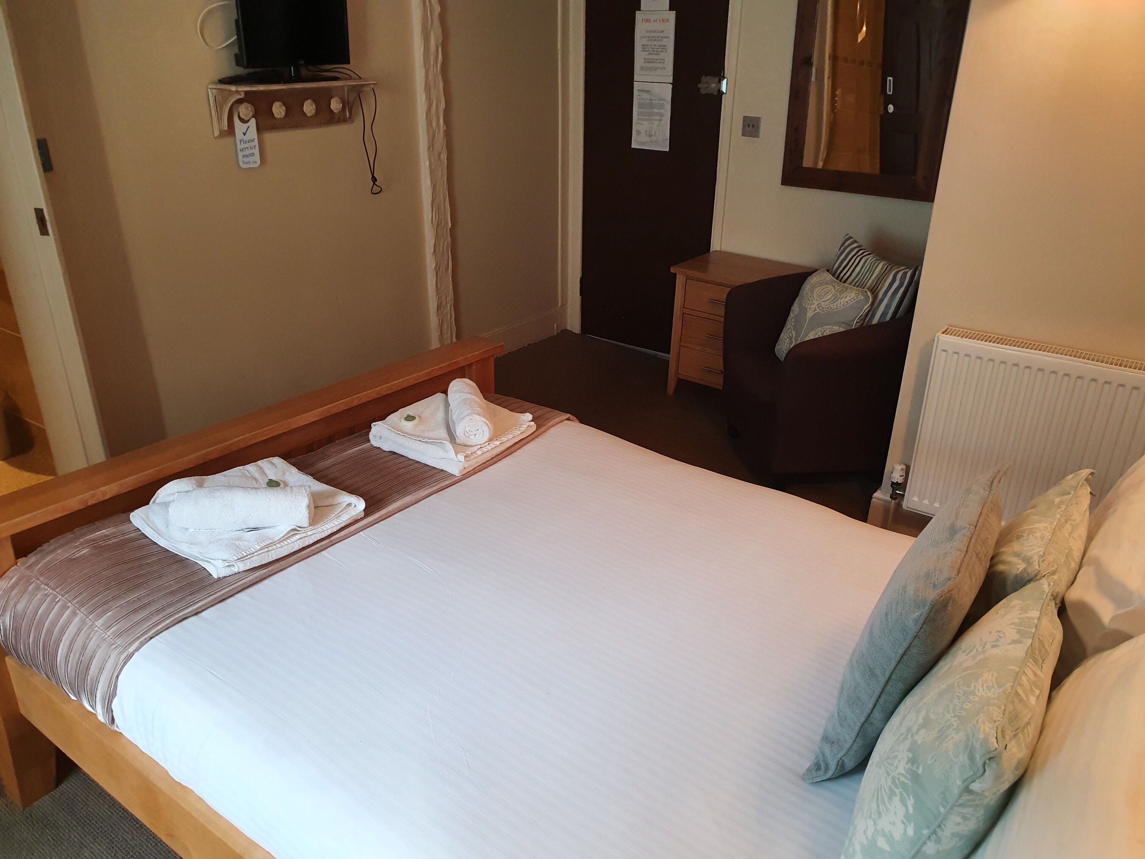 A hotel room with a bed, a small table, a chair, a TV, and a radiator.