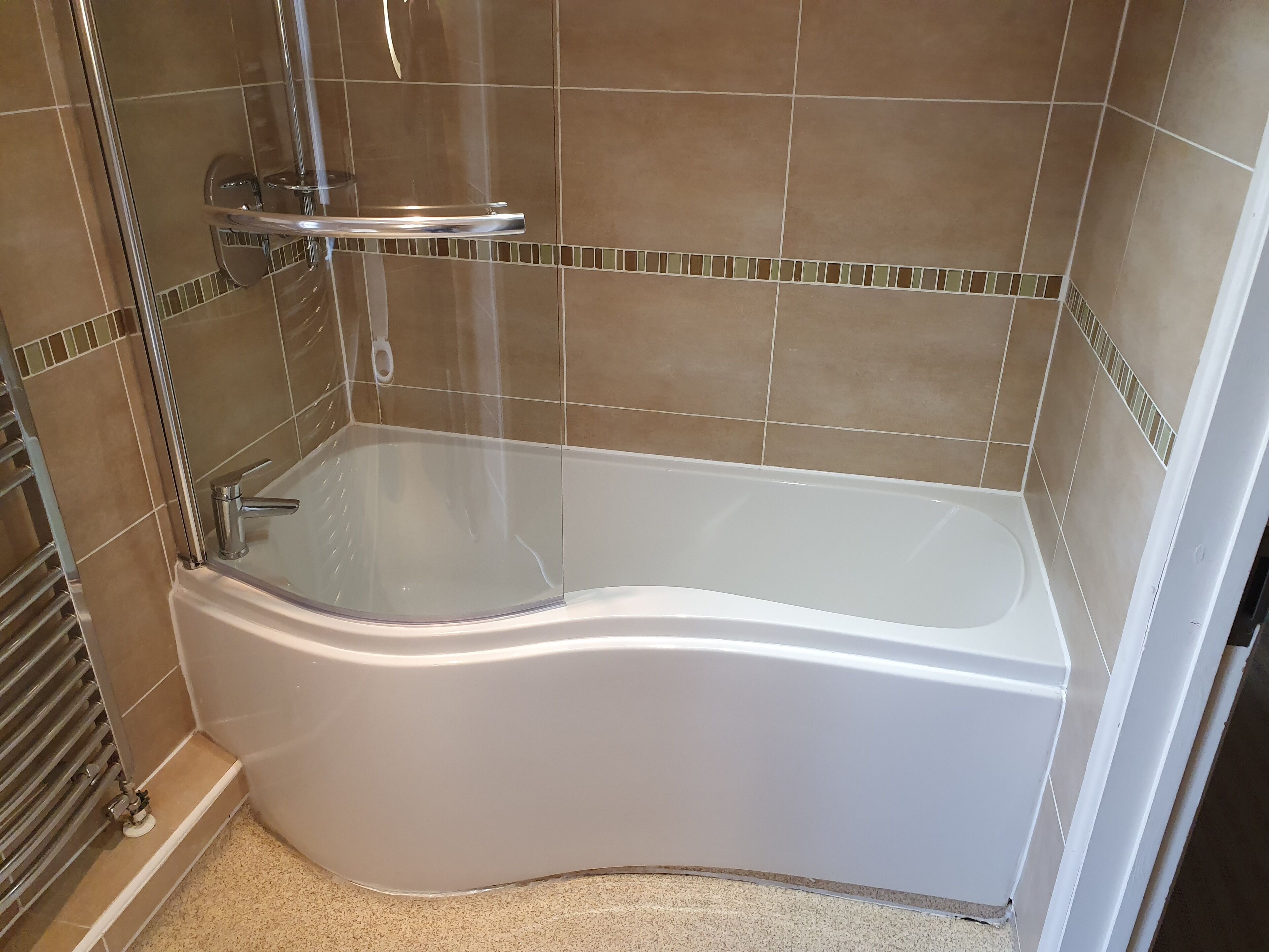 Une douche d’angle avec un pare-douche en verre, des accessoires chromés et un mur carrelé.