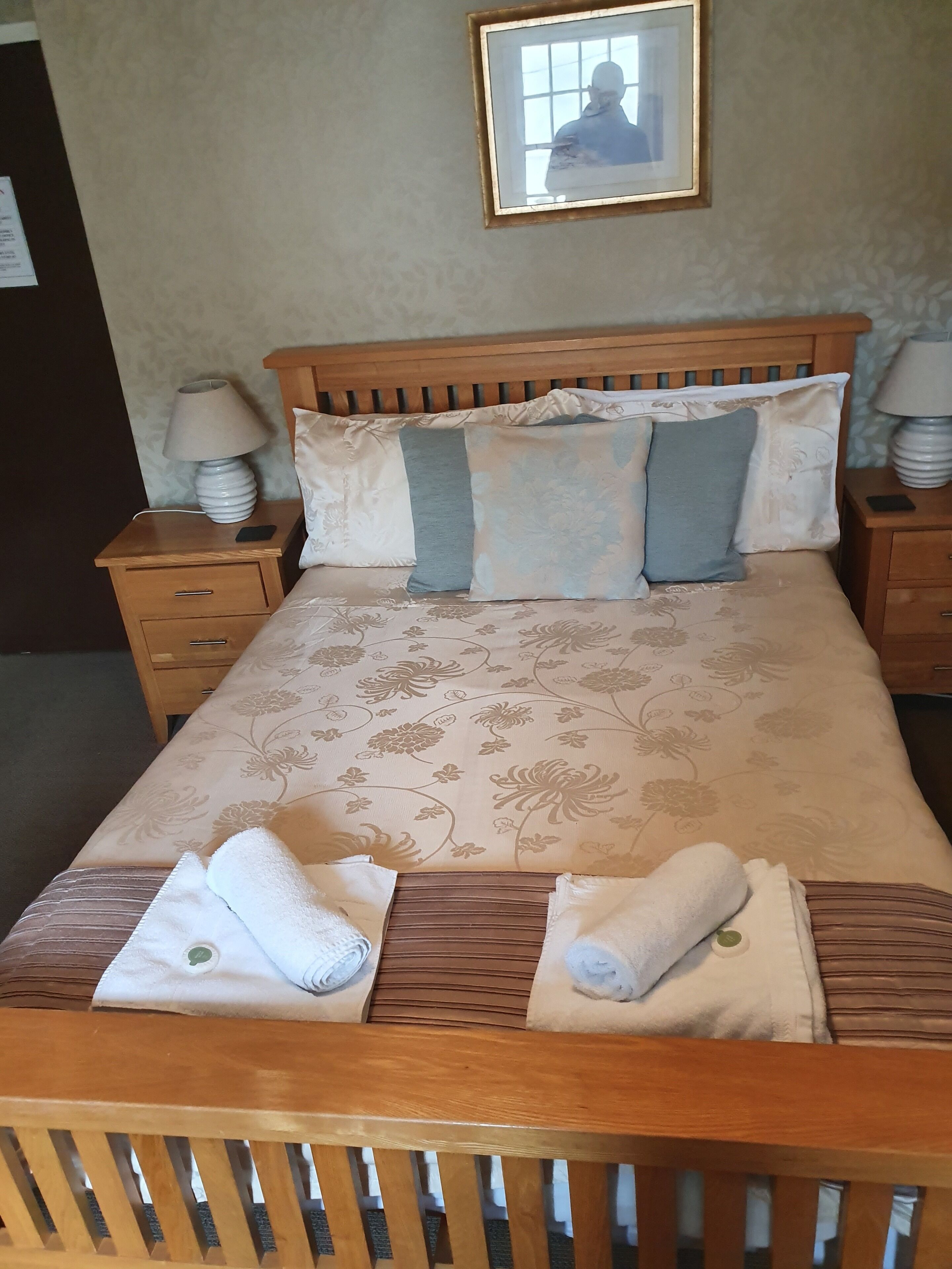A neatly made bed with floral bedding, two bedside tables with lamps, and a framed picture on the wall.