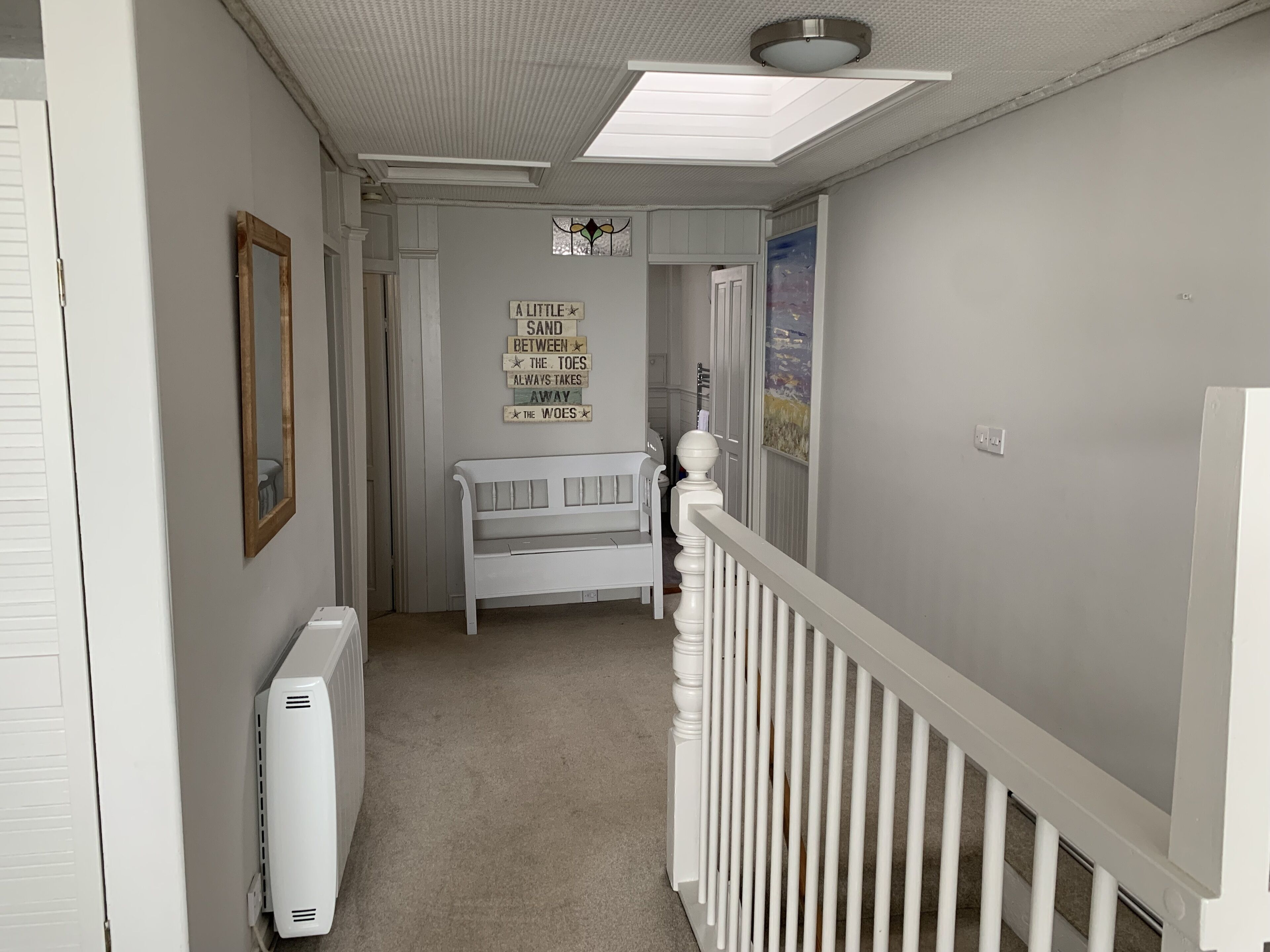 Um corredor estreito com um radiador branco, um banco branco e um lustre no teto.