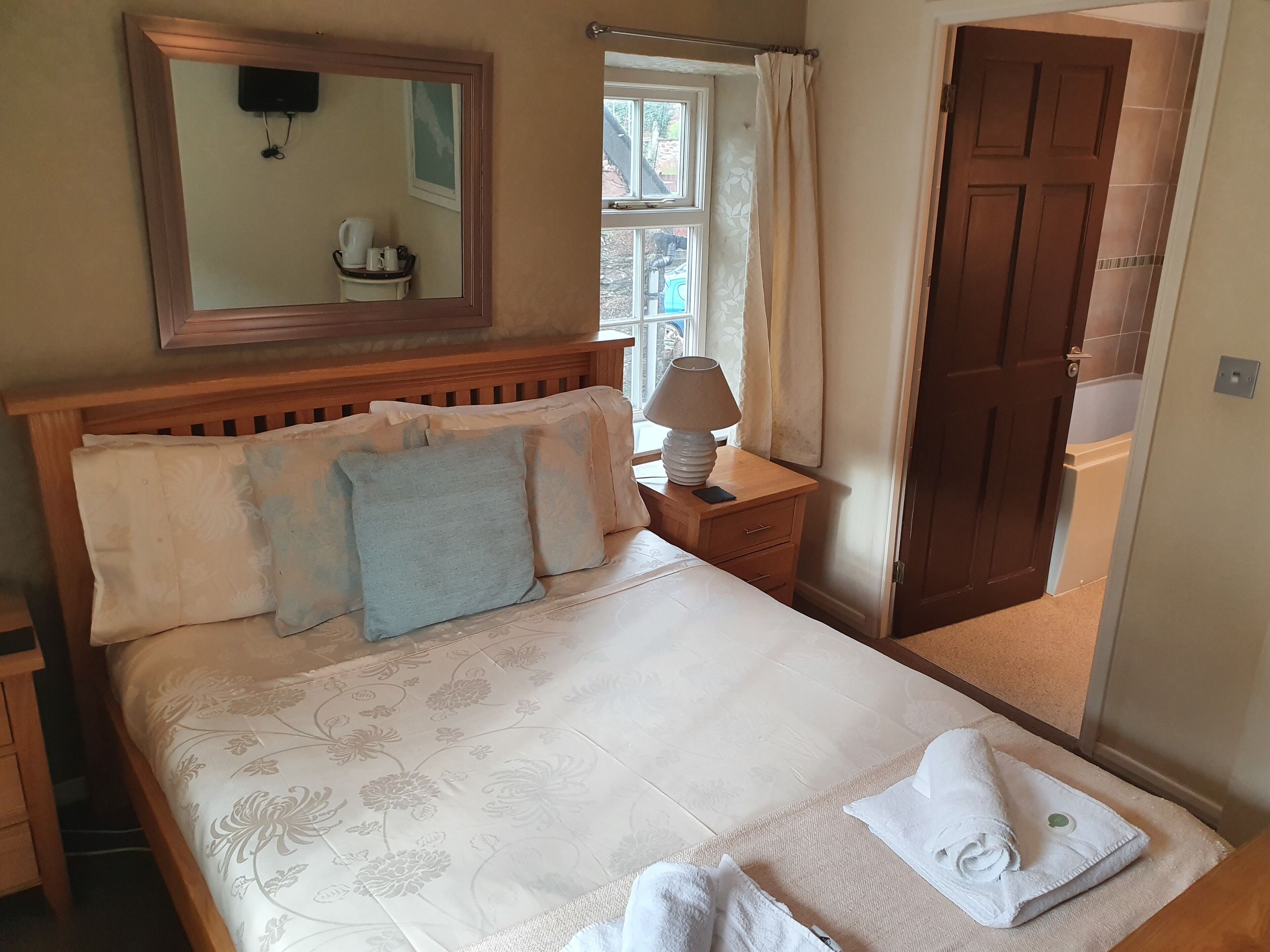 A neatly made bed with floral bedding, a bedside lamp, and a towel on the floor.