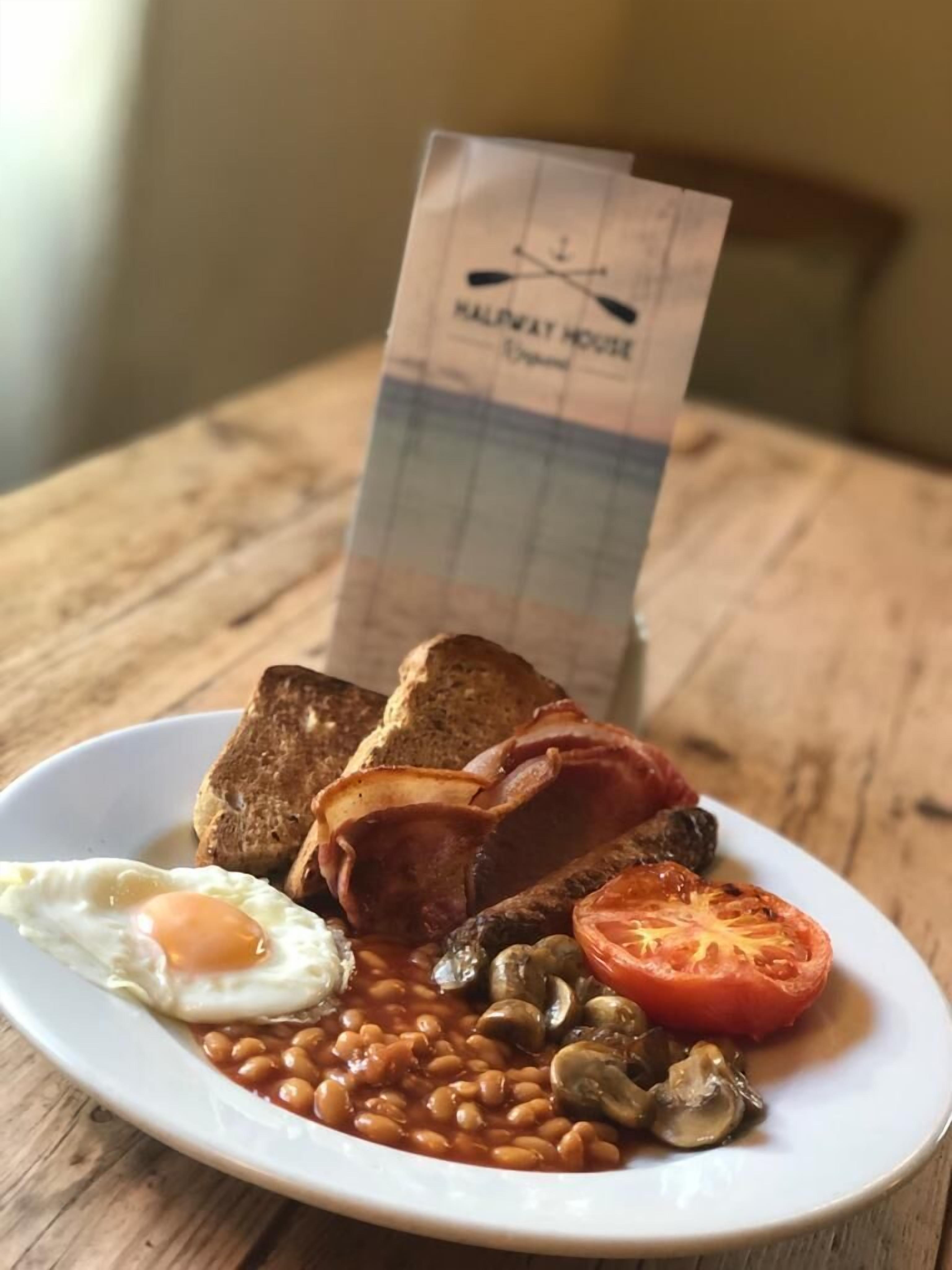 Une assiette de nourriture pour le petit-déjeuner comprenant des toasts, du bacon, des œufs, des haricots, des champignons et une tomate.