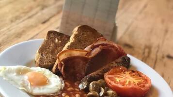 Une assiette de nourriture pour le petit-déjeuner comprenant des toasts, du bacon, des œufs, des haricots, des champignons et une tomate.