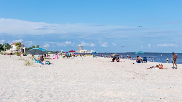 Una playa con sombrillas, gente tomando el sol y un edificio al fondo.