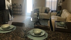 Un comedor con una mesa preparada para cuatro personas, un sofá y un televisor al fondo.