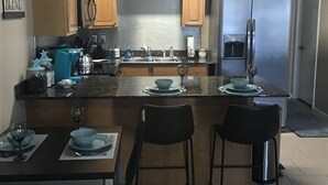 Cocina moderna con armarios de madera, refrigerador de acero inoxidable y una barra con taburetes.