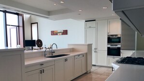 Une cuisine moderne avec des meubles blancs, un grand îlot central doté d’un évier et des appareils électroménagers intégrés.